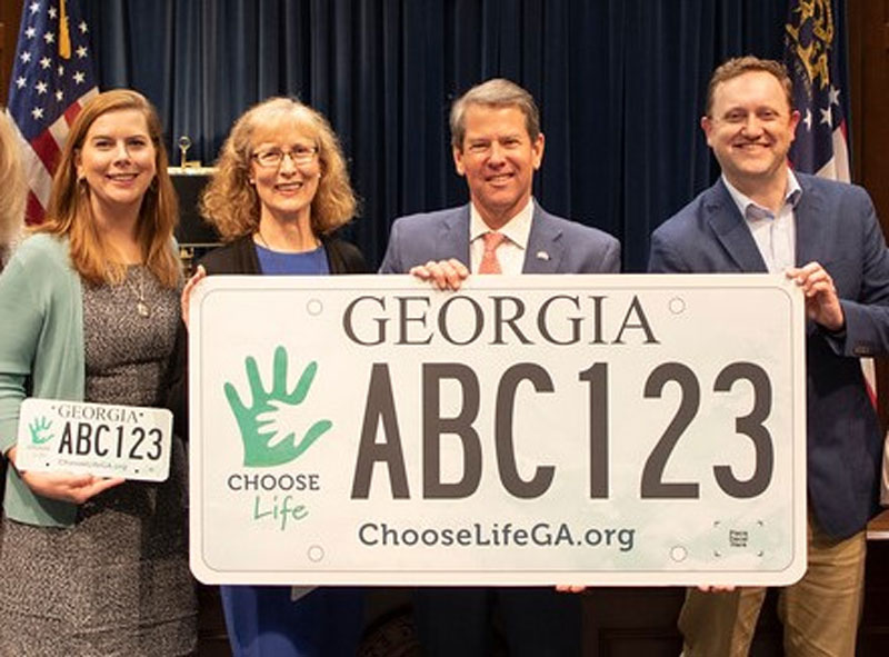 Choose Life board member Amy Shirley, left, joins president Karen LaBarr and graphic designer Adam Houston in unveiling the new Choose Life license plate to Governor Brian Kemp.