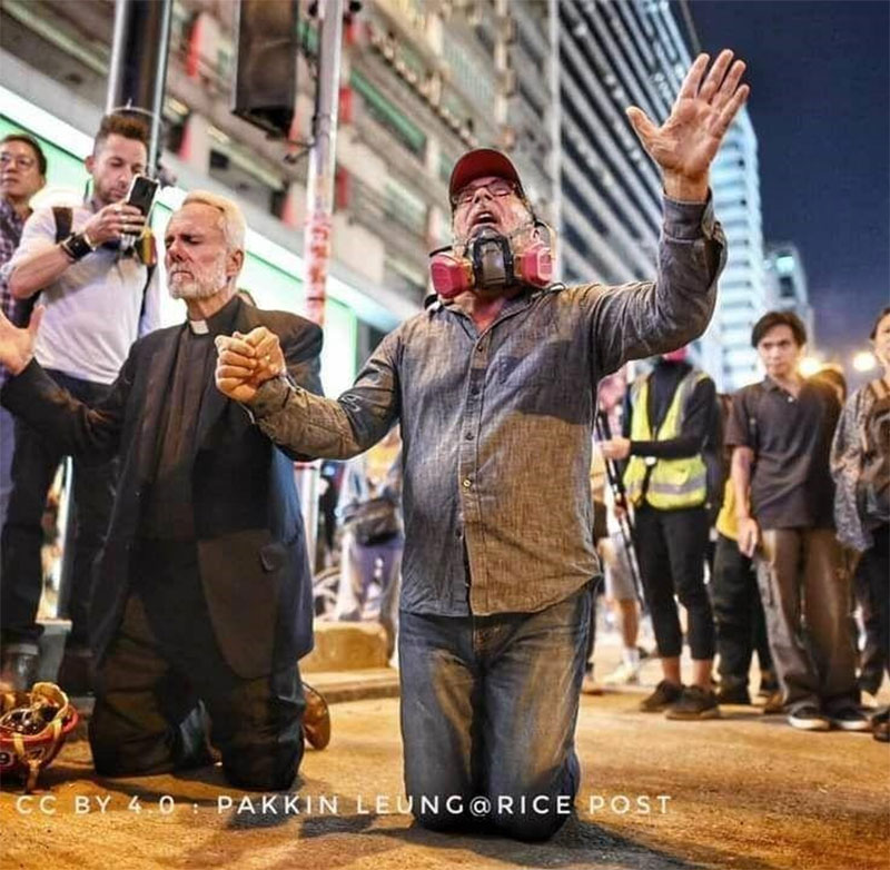 2019 photo of Rev. Mahoney (right) praying on the streets of Hong Kong with thousands of students for freedom during the 